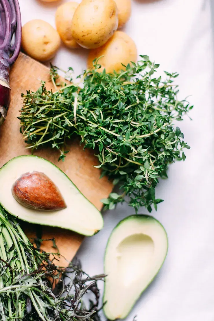 An avocado and other leafy substances sit on a table