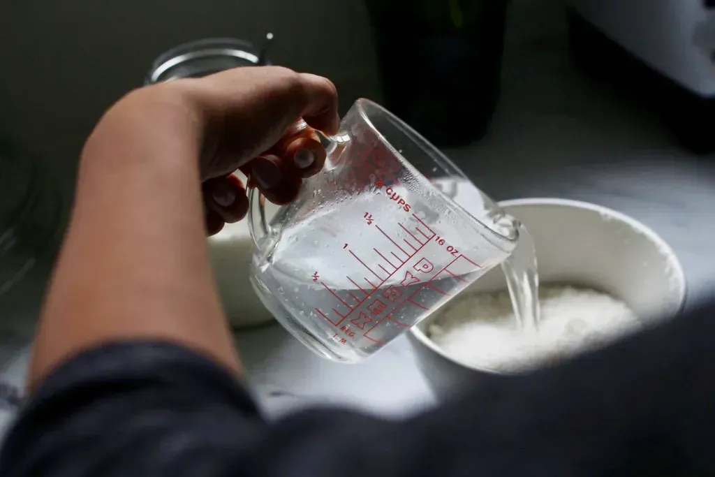 A person pours water from a measuring cup into a bowl