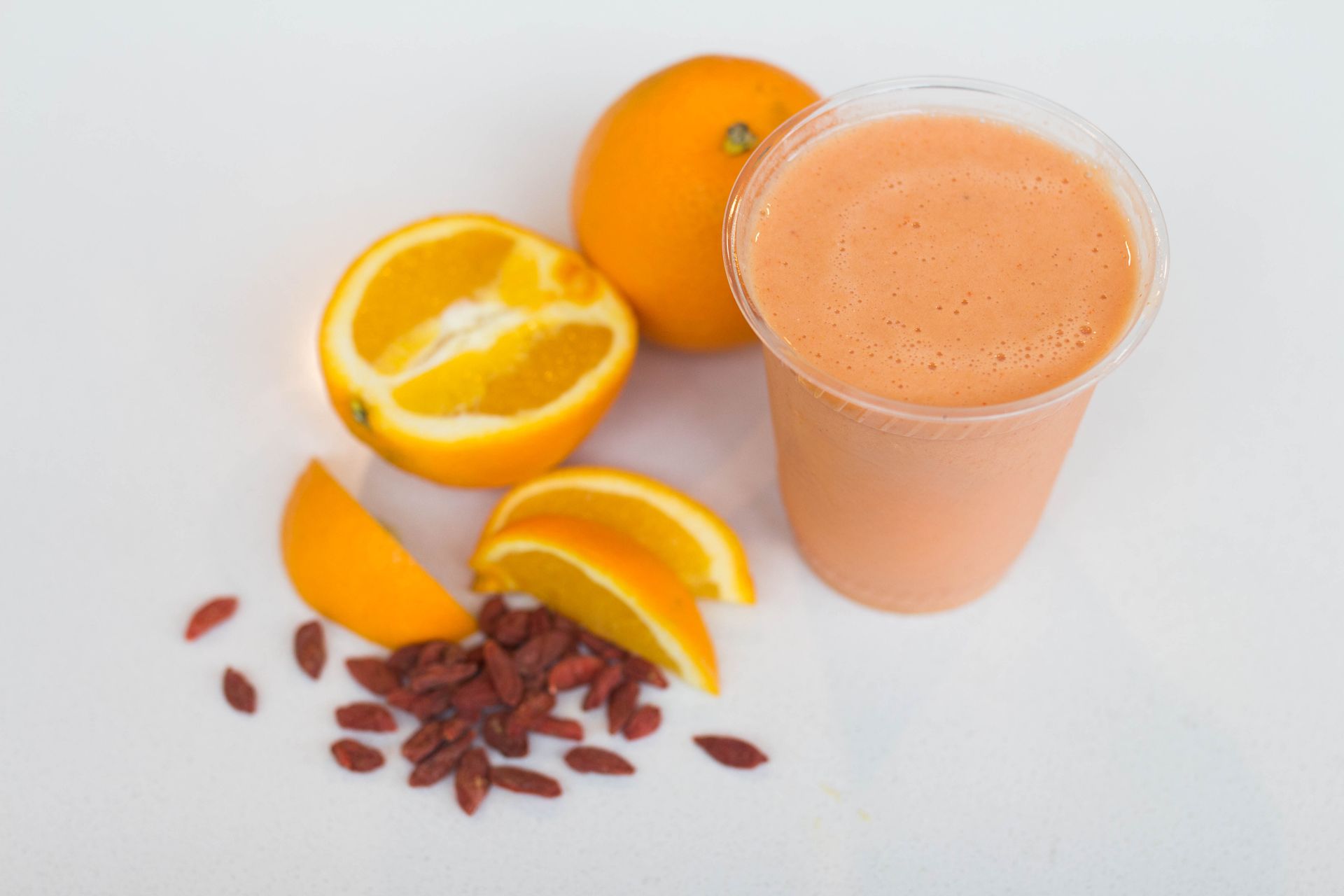 Cut up oranges and nuts sit on a table next to an orange smoothie in a glass