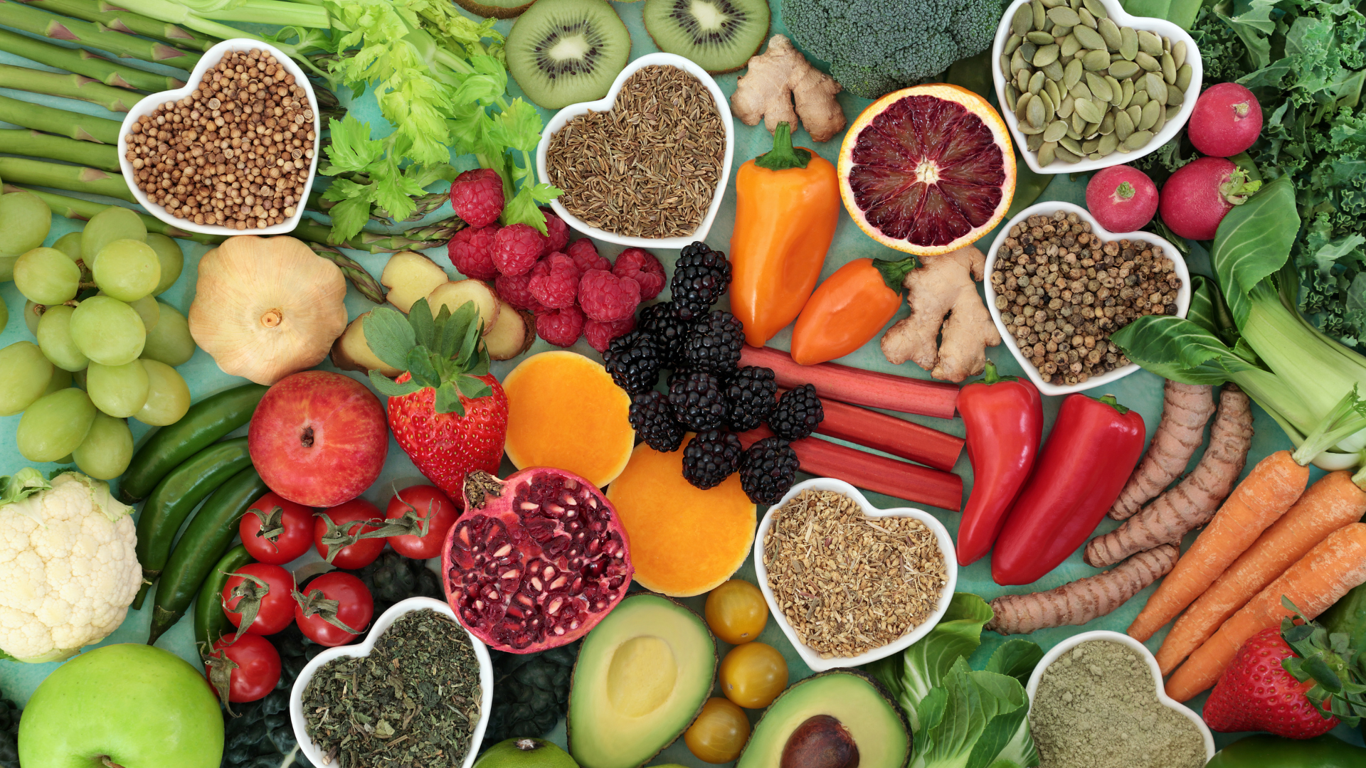 Various fruit and veggies surround a table with heart-shaped bowls filled with nuts and oats scattered about