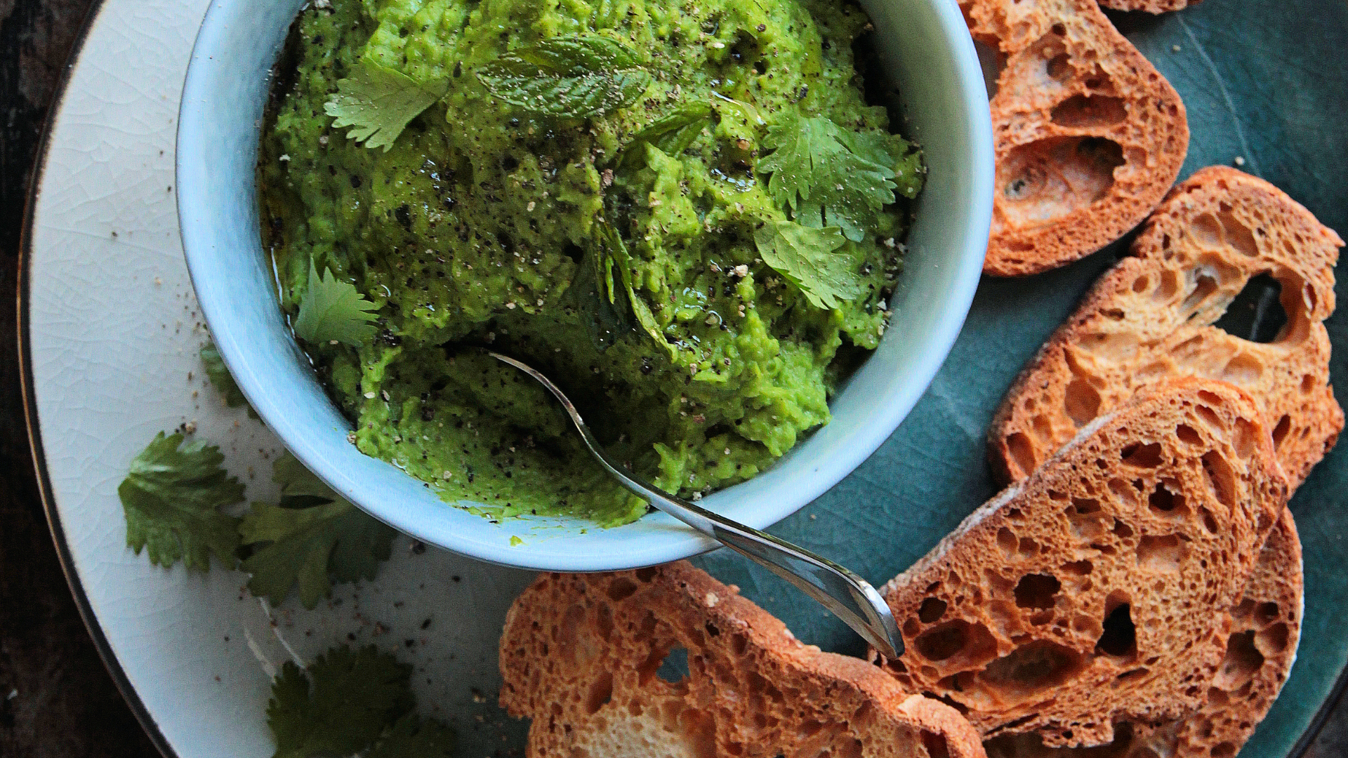 A bowl of leafy green veggies surrounded by freshly baked bread