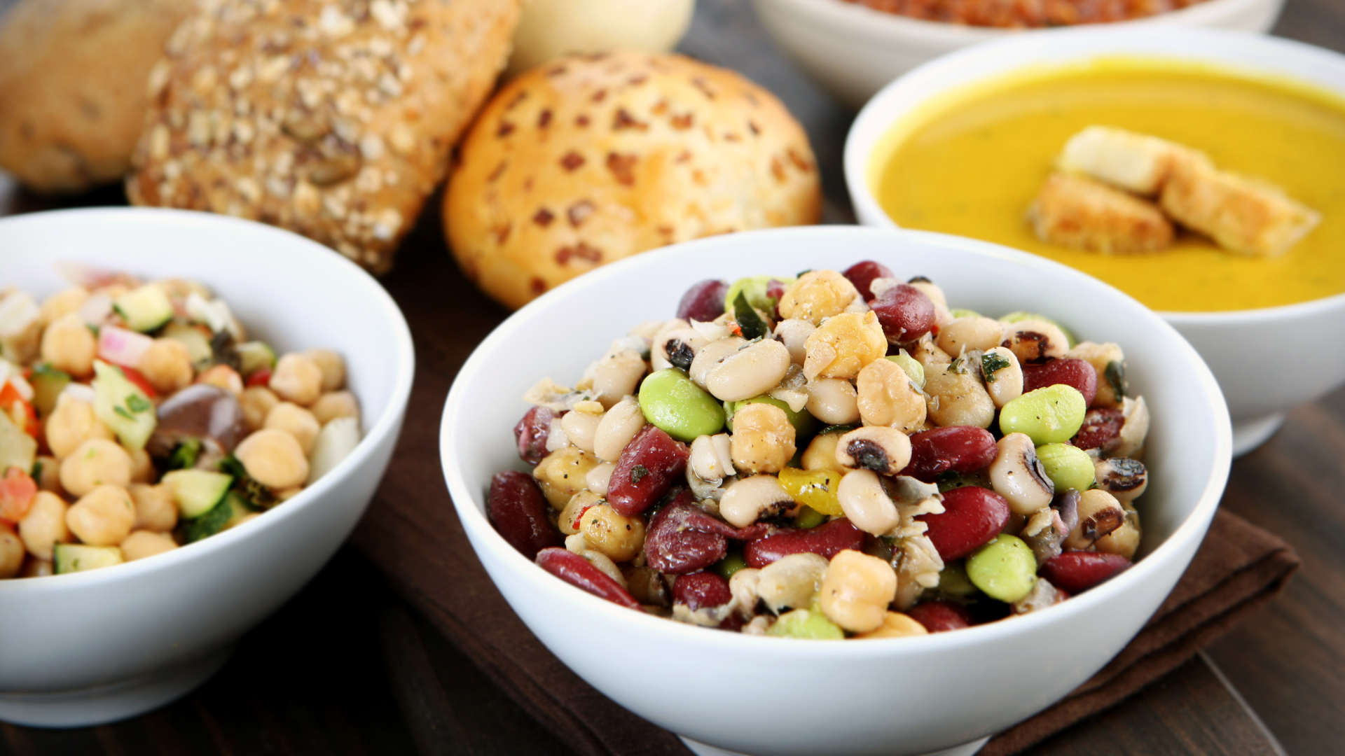 A bowl of mixed nuts sits next to bowl carrying identical items, behind the bowls is a bowl of soup and bread