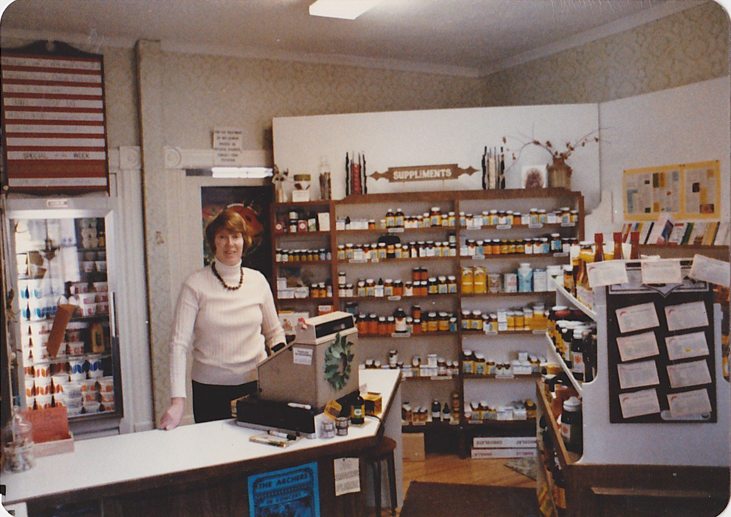 An old photo woman stands at a cash register with various products behind her