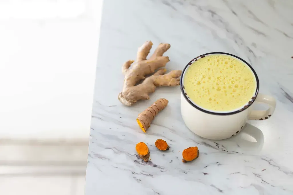 A glass mug of tea sits on a table with raw ginger sitting underneath