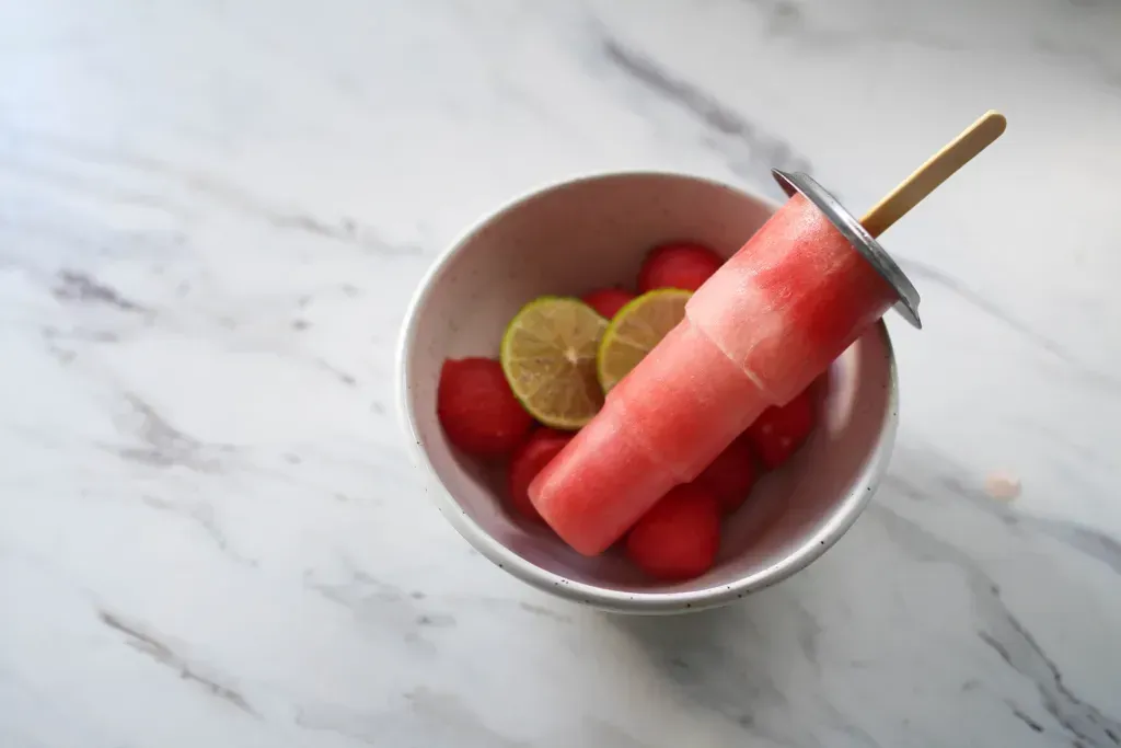a popsicle sits in a bowl with other fruit surrounding it