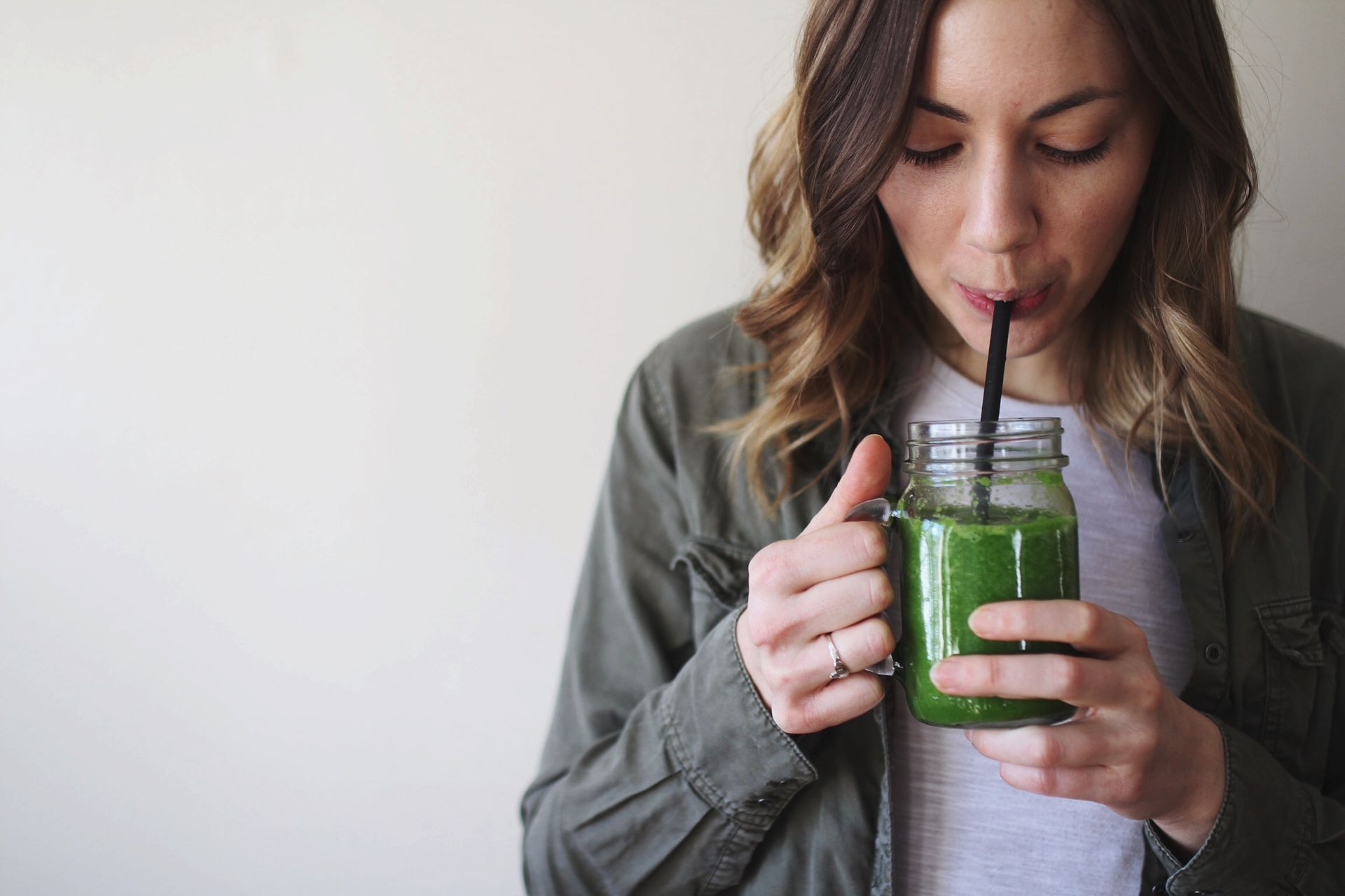 woman drinking a green smoothie from a glass jar with a straw