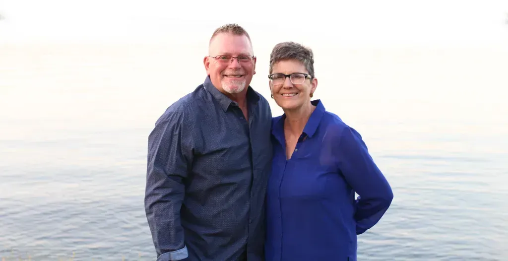 A man and a woman stand in front of a large body of water