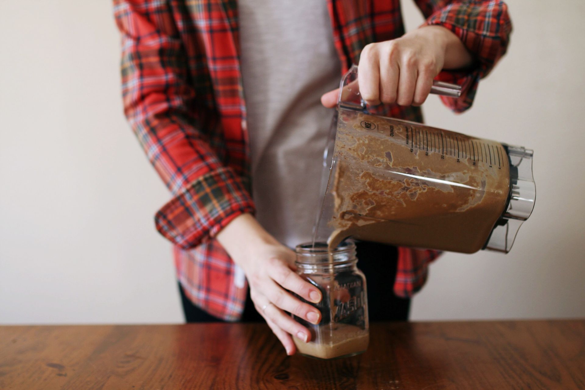 A person pours a protein shake from a blender into a glass