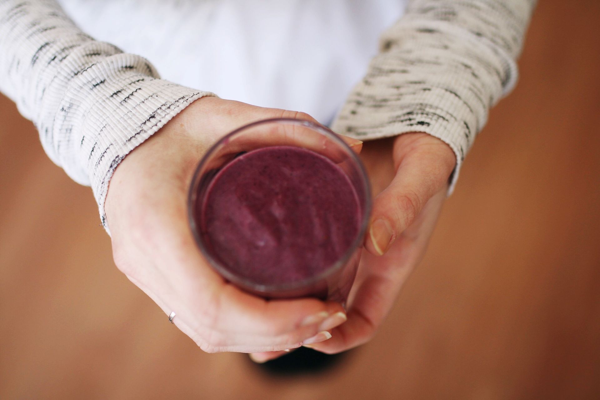 An aerial view of a person holds a purple smoothie in a glass