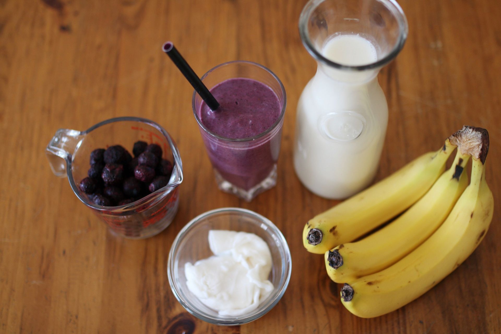 Various smoothie ingredients like berries and bananas sit on a table