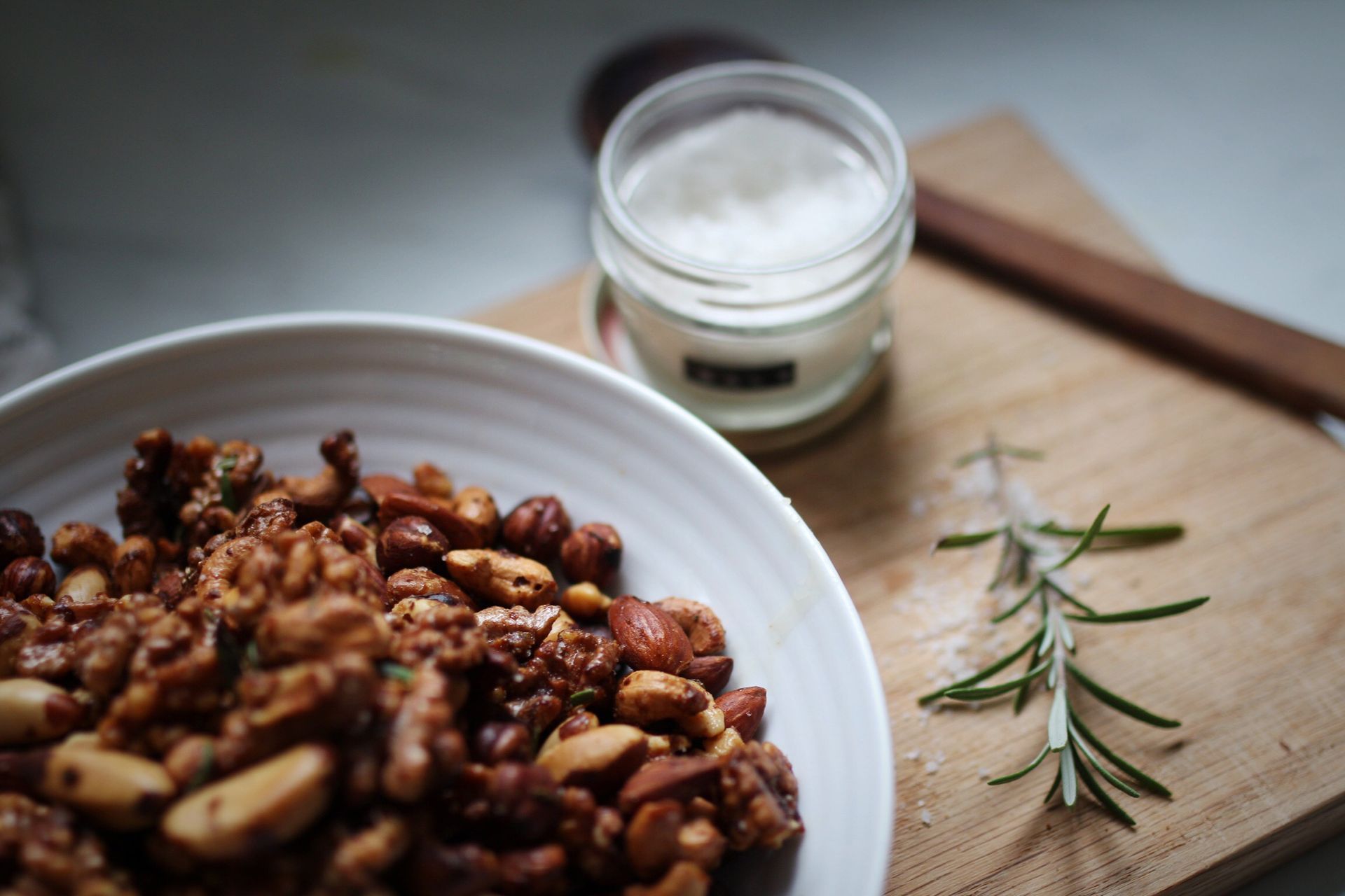 A plate filled with mixed nuts sits on top of a cutting board with a small container of a white substance