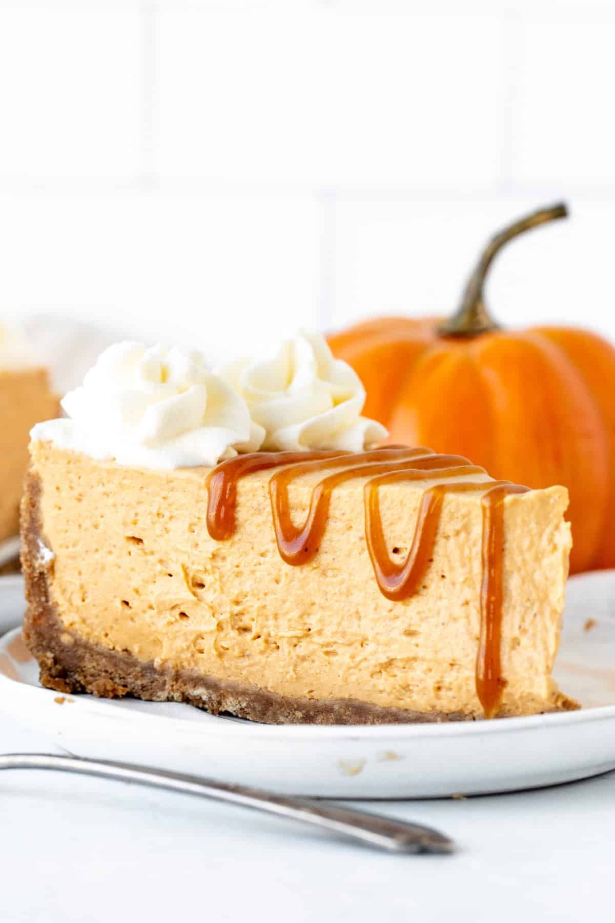 A no-bake pumpkin cheesecake sits on a plate with an orange pumpkin in the back.