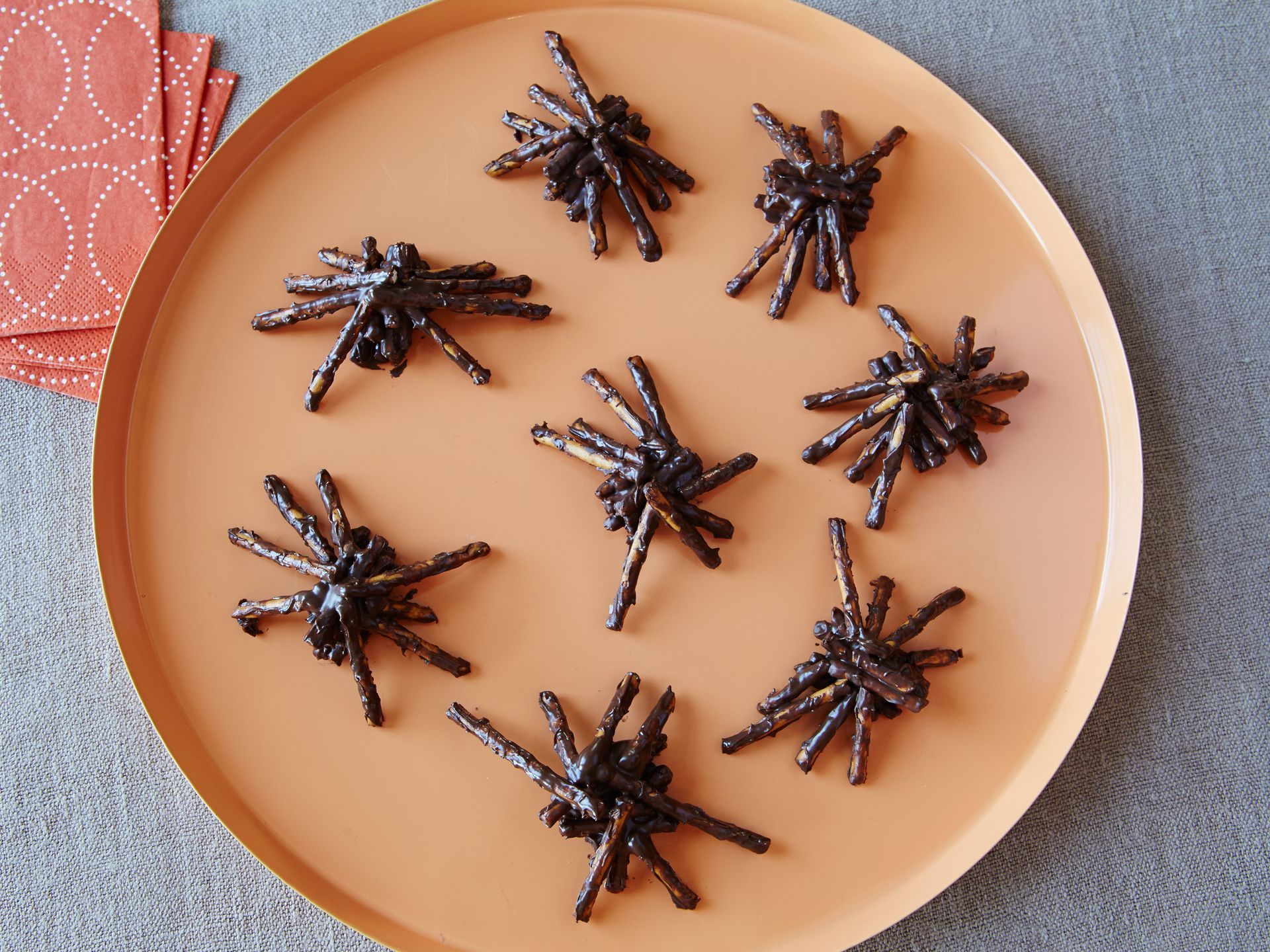 Halloween treats made to look like little spiders sitting on an orange plate with red napkins to the side