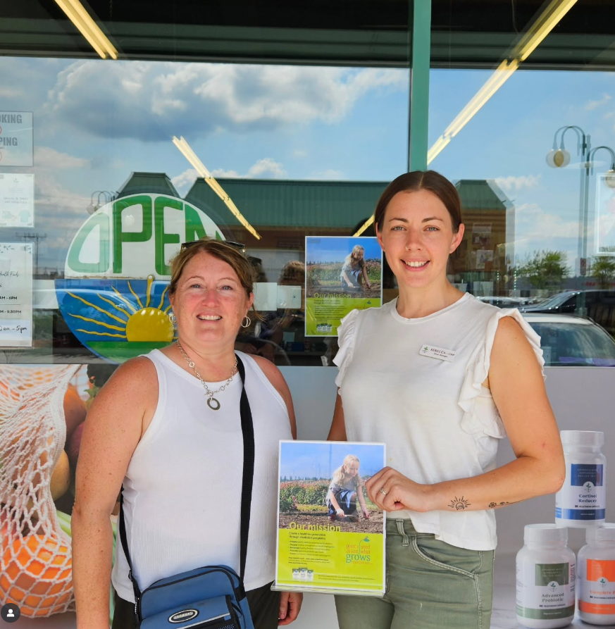 Two women stand in front of our Jo Anne's Place Store in Lindsay Ontario wearing white shirts and smiling