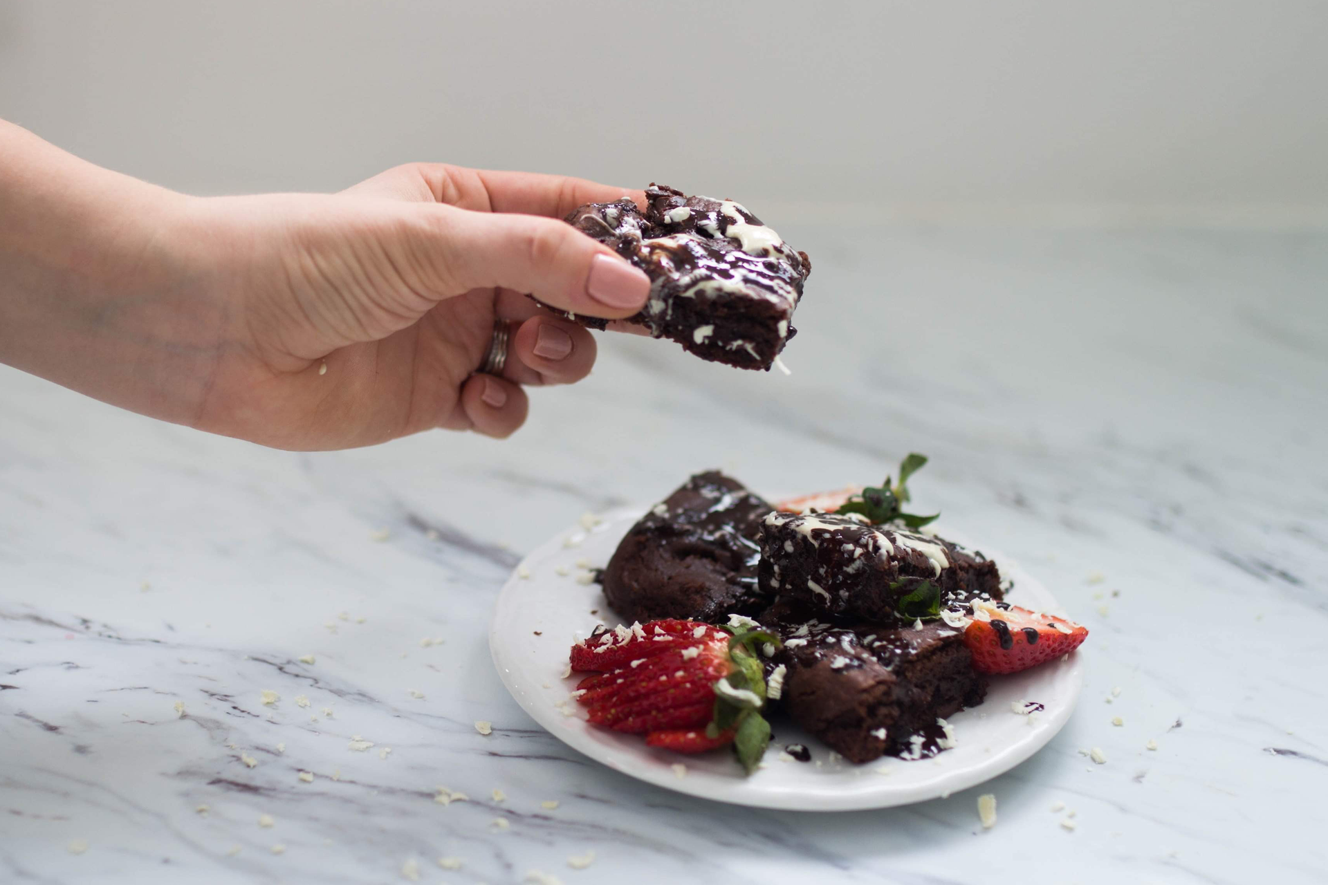 a person holds up a chocolate brownie above a plate of other brownies and fruit