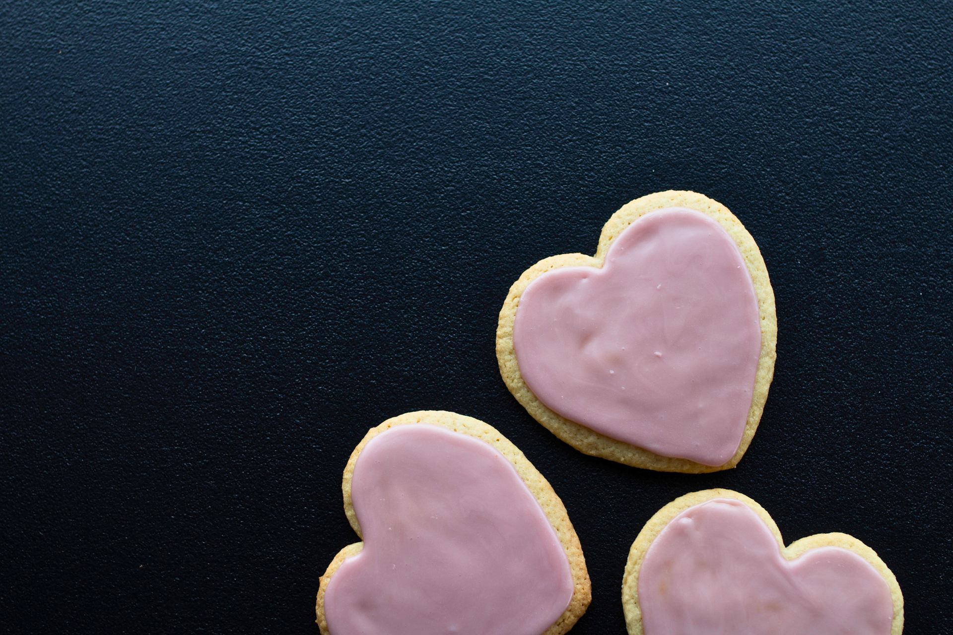 Heart shaped cookies with pink frosting sit on a dark blue counter