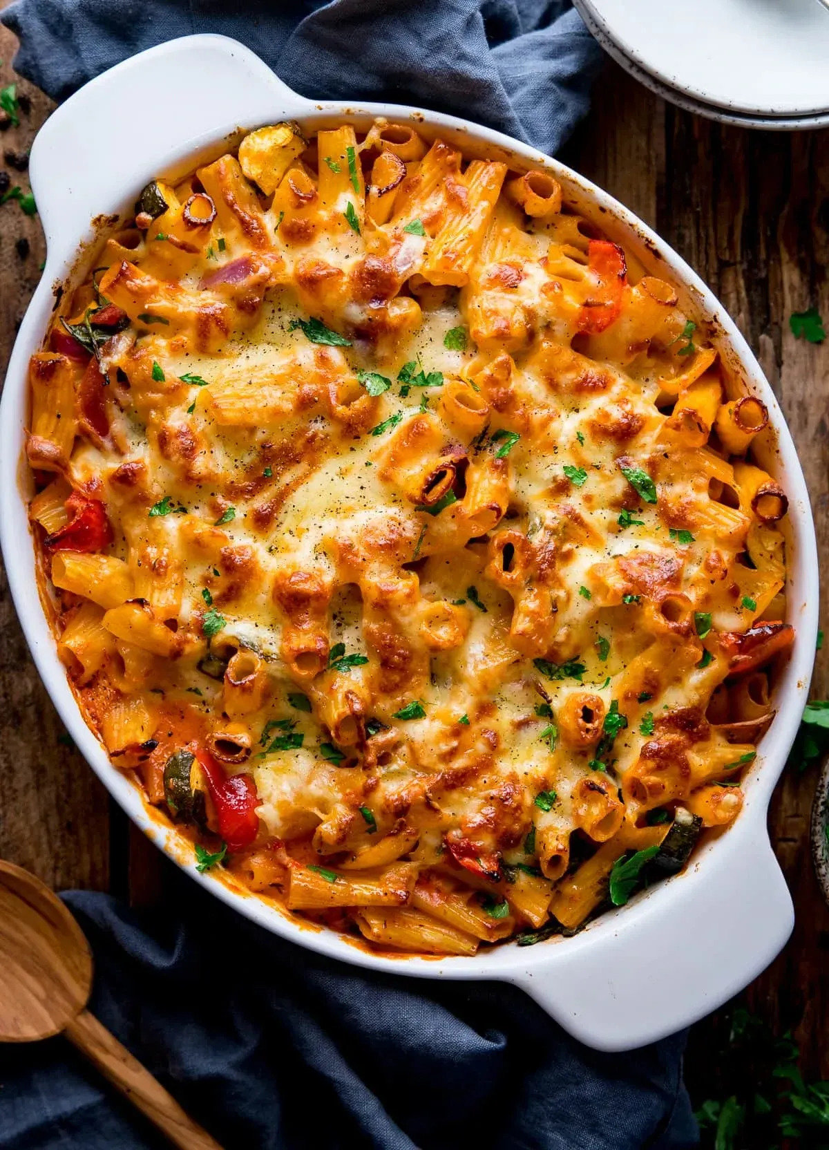 A pasta dish sits inside an over-ready tray, having just being baked and looking cheesy and filled with whole foods