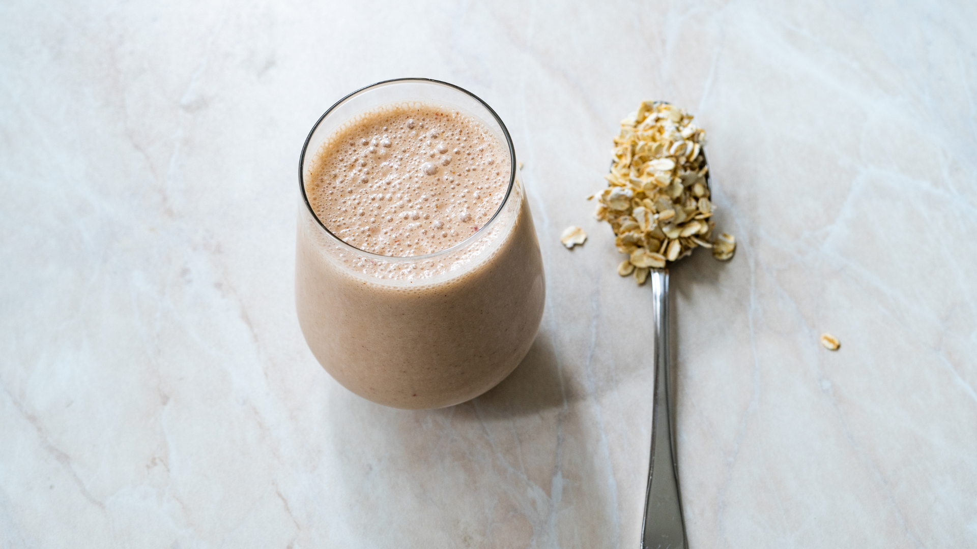 a glass containing a smoothie and a spoon full of oats placed next to it
