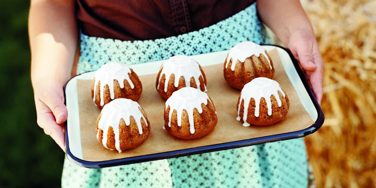 A person holds a tray of Apple Cardamom Cakes with Apple Cider Icing melting off the top and dripping to the bottom