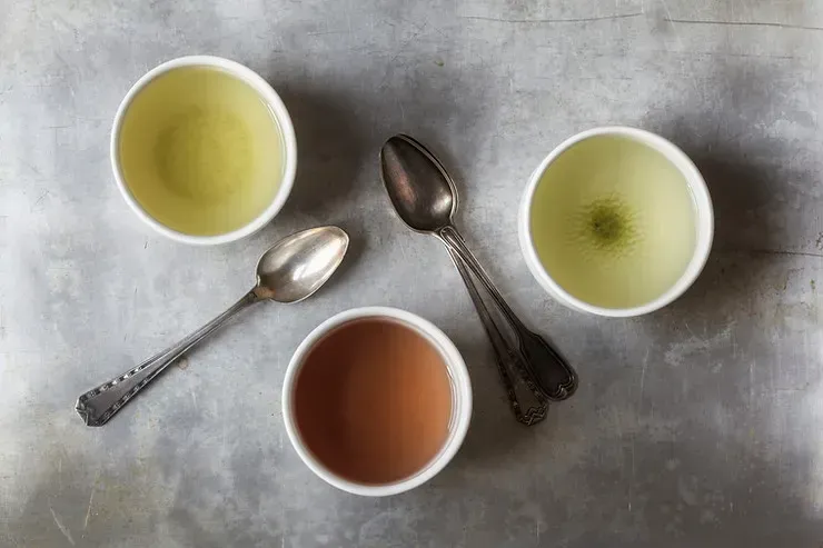 Various bowls of soup sit on a table with metal spoons in-between