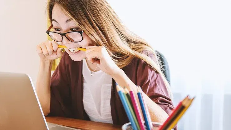 A woman bites her pencil in nervousness as she looks at her laptop screen