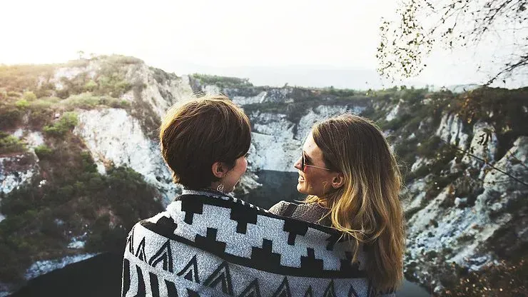 Two ladies are wrapped in a blanket together on a mountain
