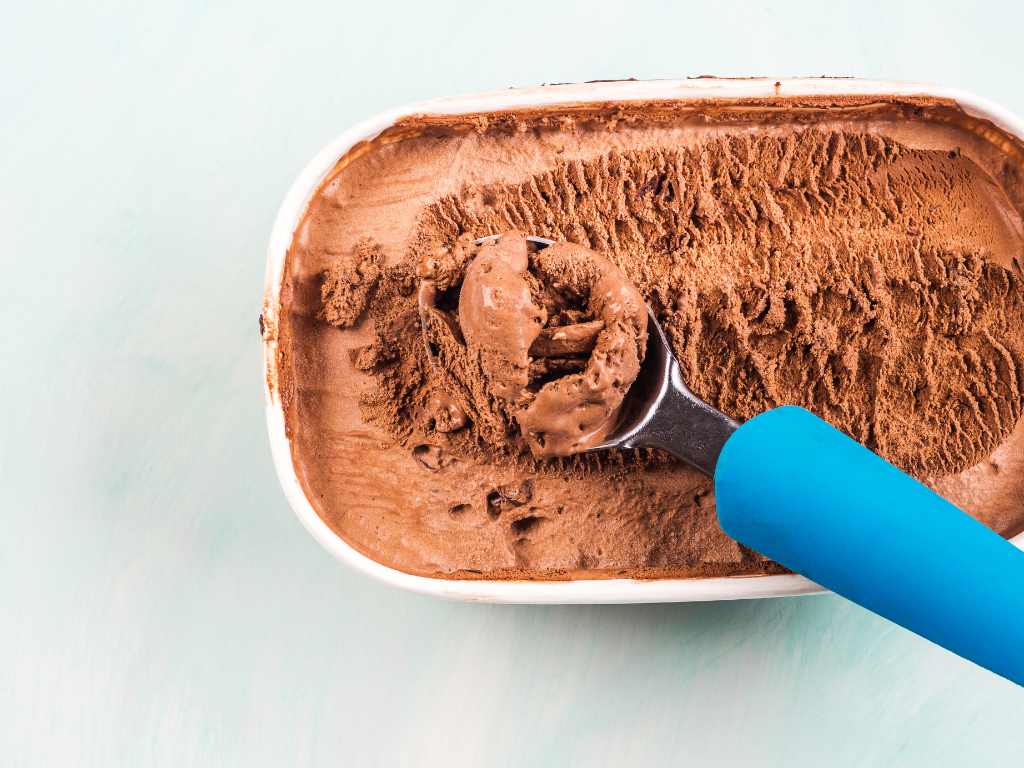 A tub of chocolate ice cream being scooped with a spoon
