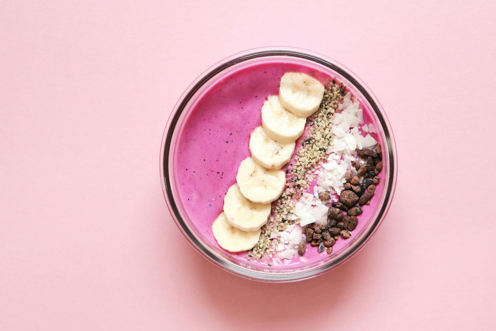 Various nuts and fruits sit inside a blender along with a pink smoothie liquid