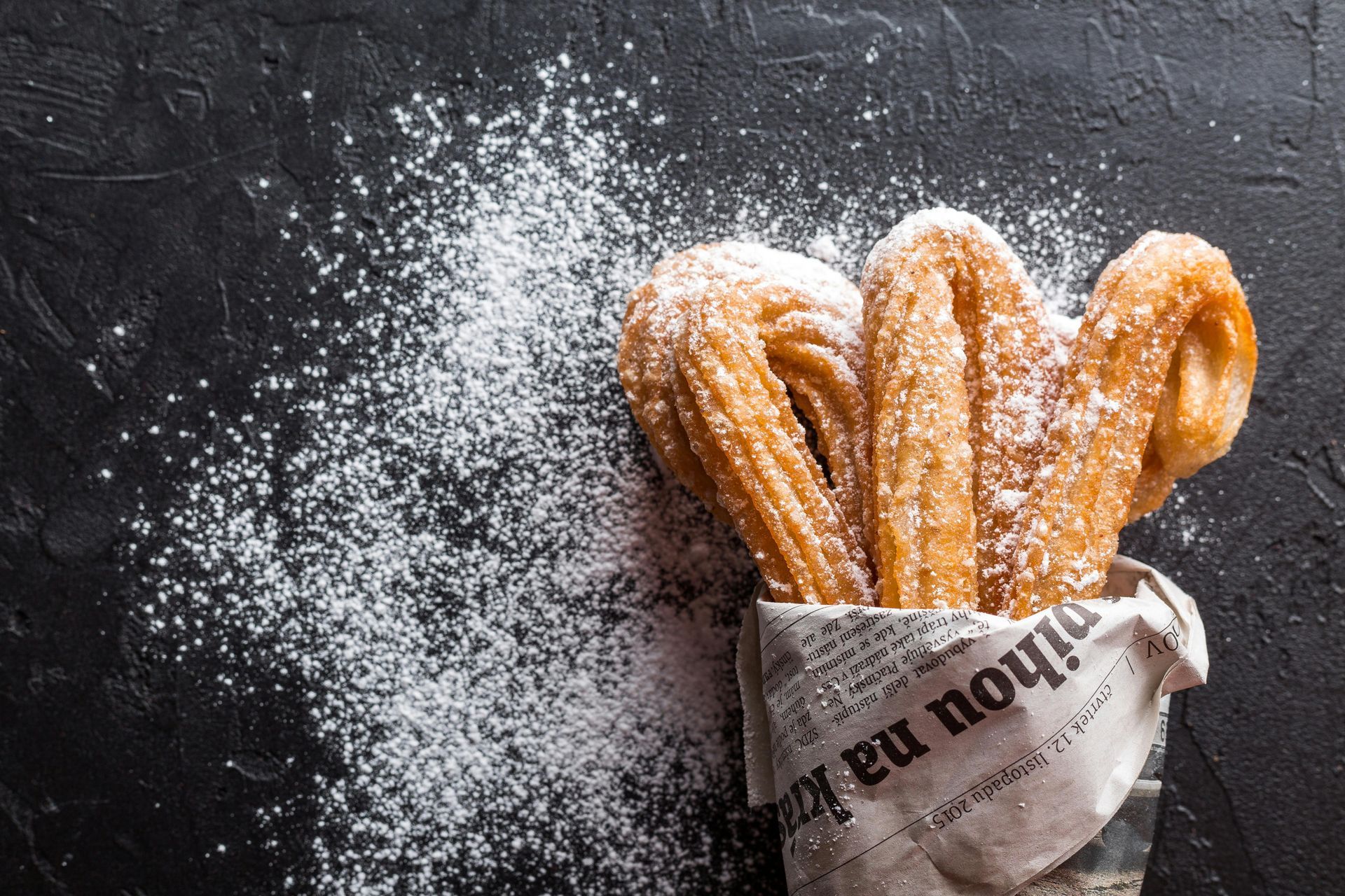 Freshly baked churros sit on a countertop with sugar poured on them