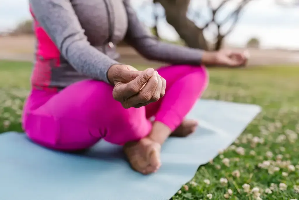 A person sits in a meditative position on a yoga mat while outside