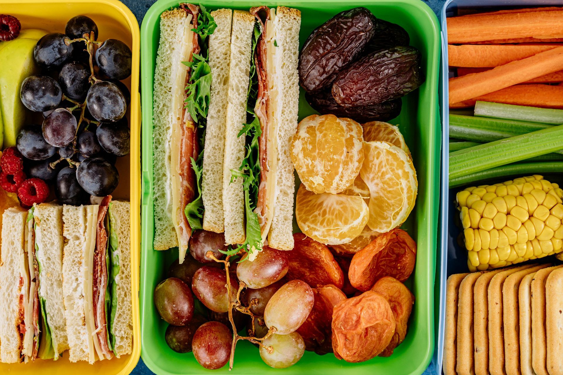 Various snack and school foods sit in a pile, sandwiches, carrots, celery and clementine's