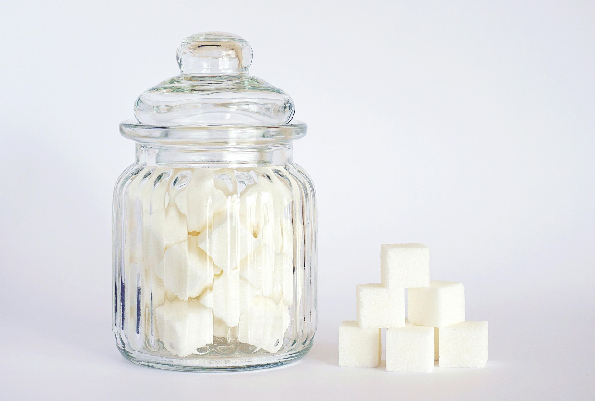 A jar containing sugar cubes and other sugar cubes sit outside of the jar