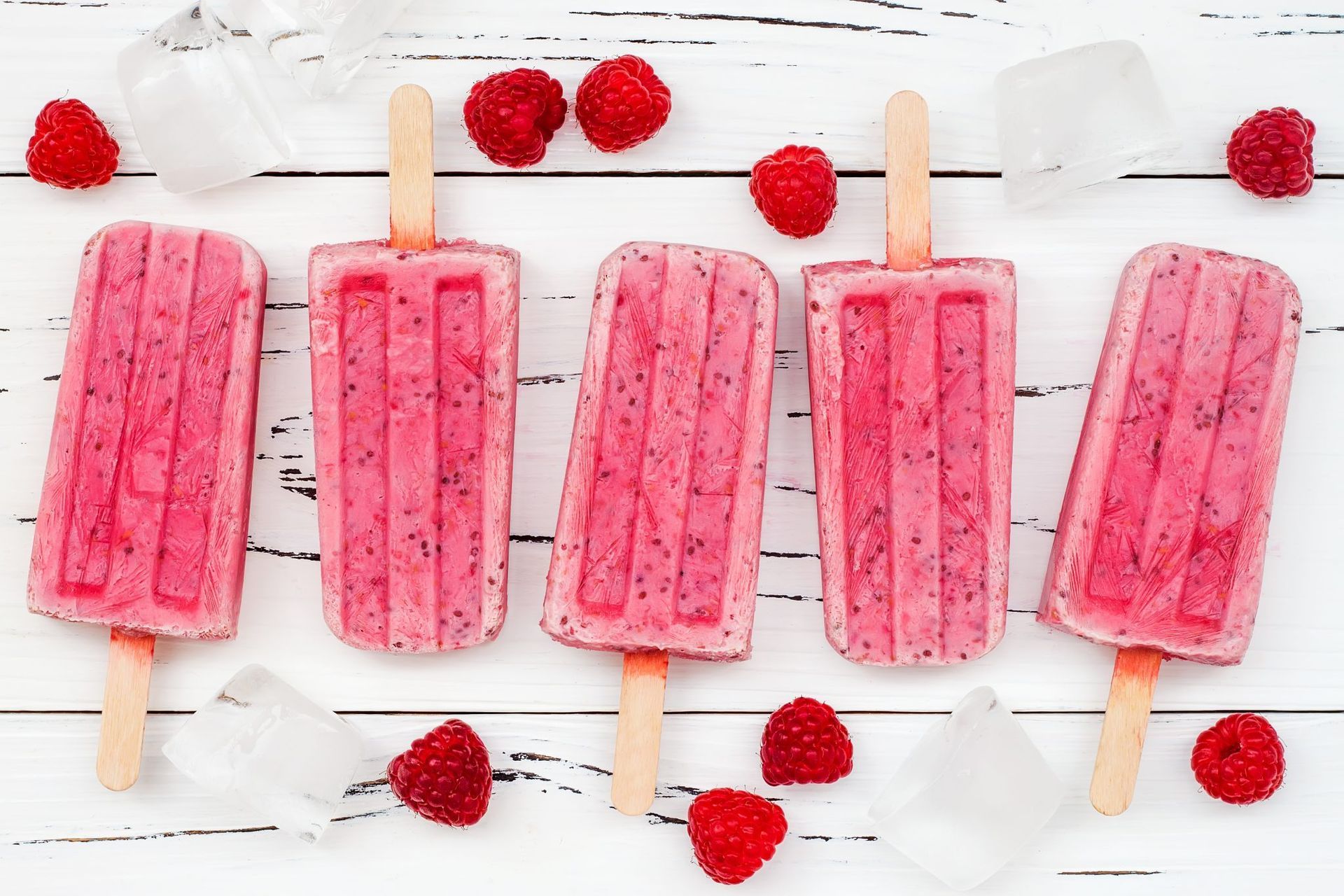 A couple razzleberry popsicles sit on a picnic table surrounded by raspberries