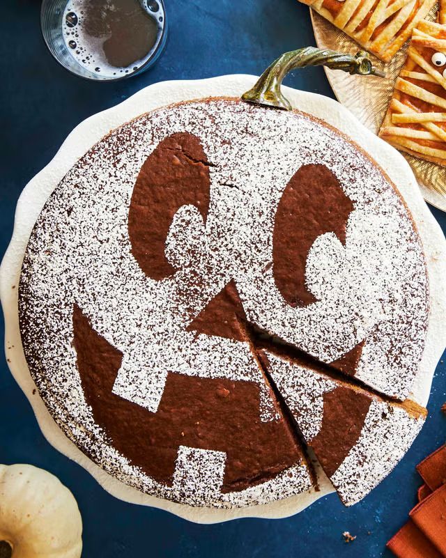 A ginger molasses cake with powdered sugar on the top made out to look like a jack-o-lantern sitting on a plate