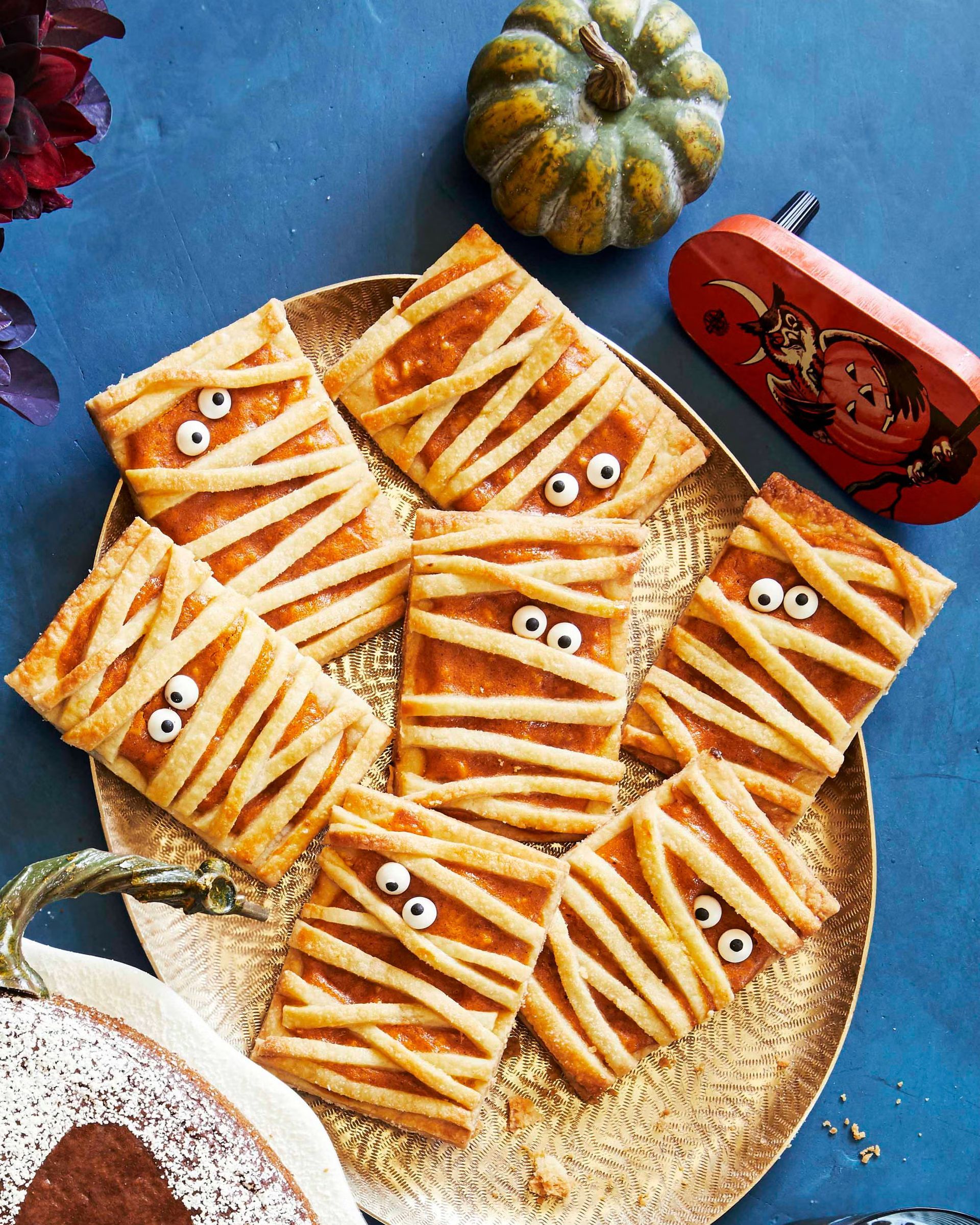 Golden, flaky hand pies that have been made to look like tiny Mummy's sitting on a gold plate against a blue background