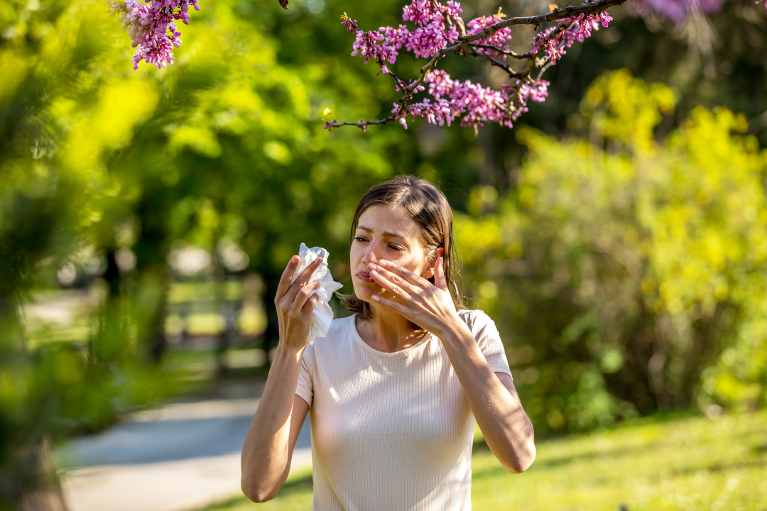A woman rubs lotion on her face while standing outside