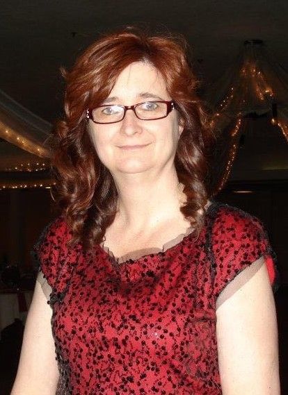 A woman wearing glasses and a red shirt is smiling for the camera.
