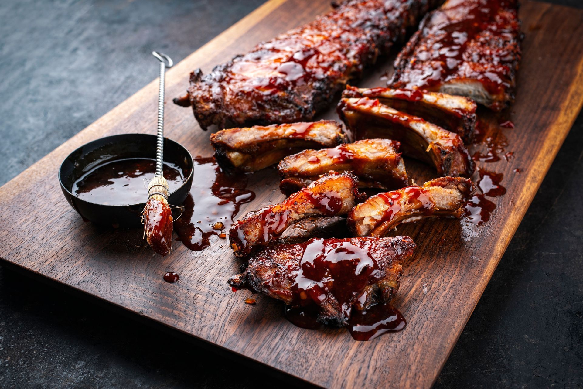 A wooden cutting board topped with ribs and a bowl of barbecue sauce