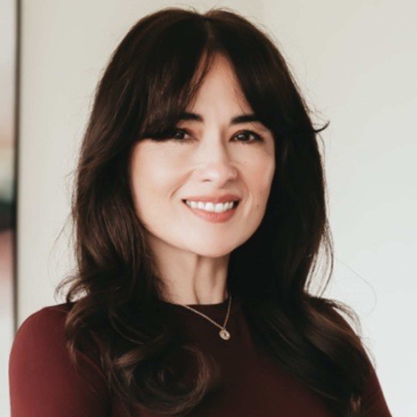 Portrait of a smiling woman with dark hair in a burgundy top against a light background