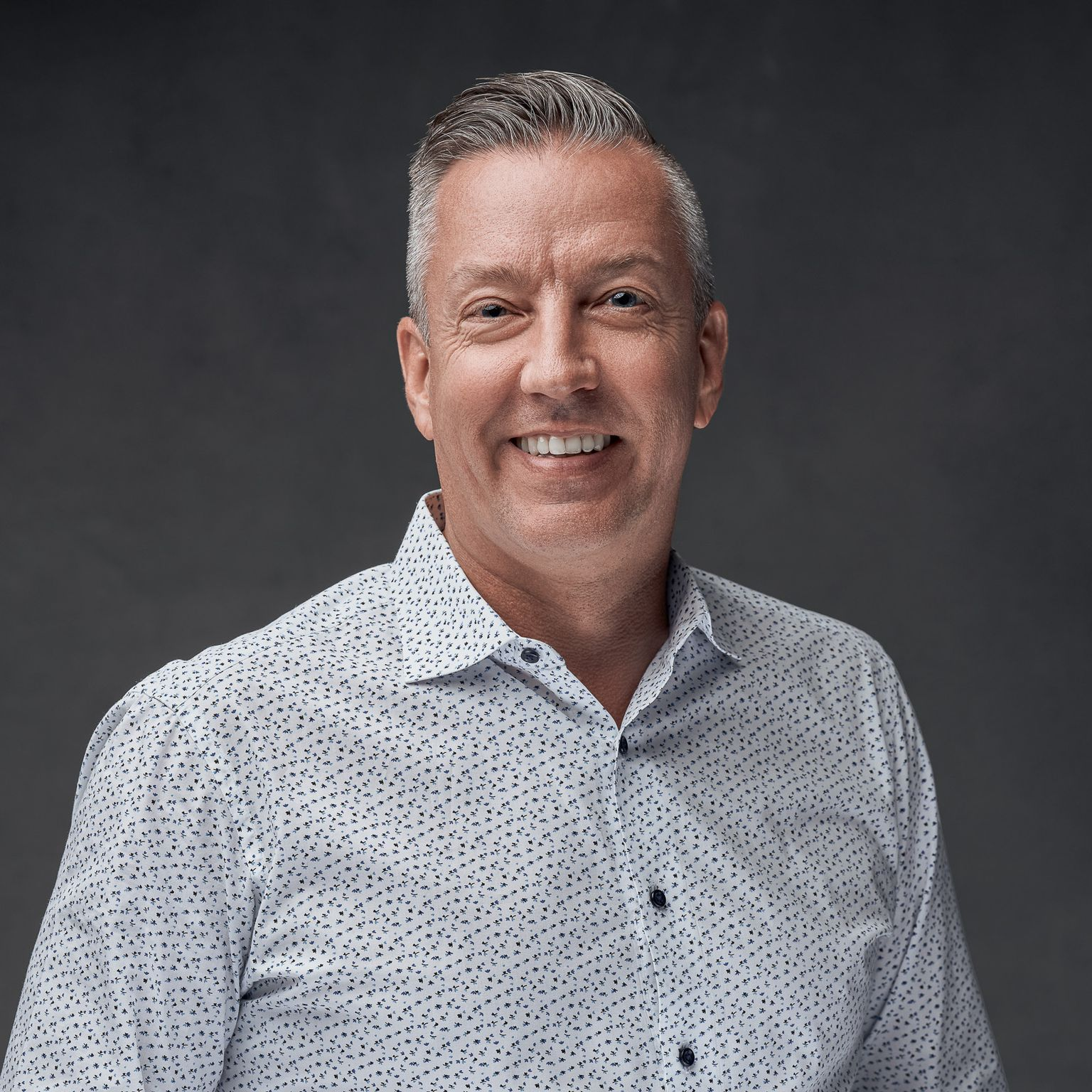 Smiling man in a white patterned shirt against a dark gray background