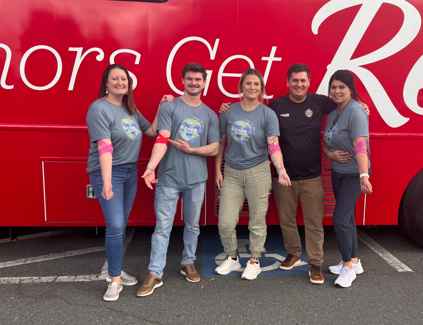 Five people in gray shirts posing in front of a red bus with white lettering.