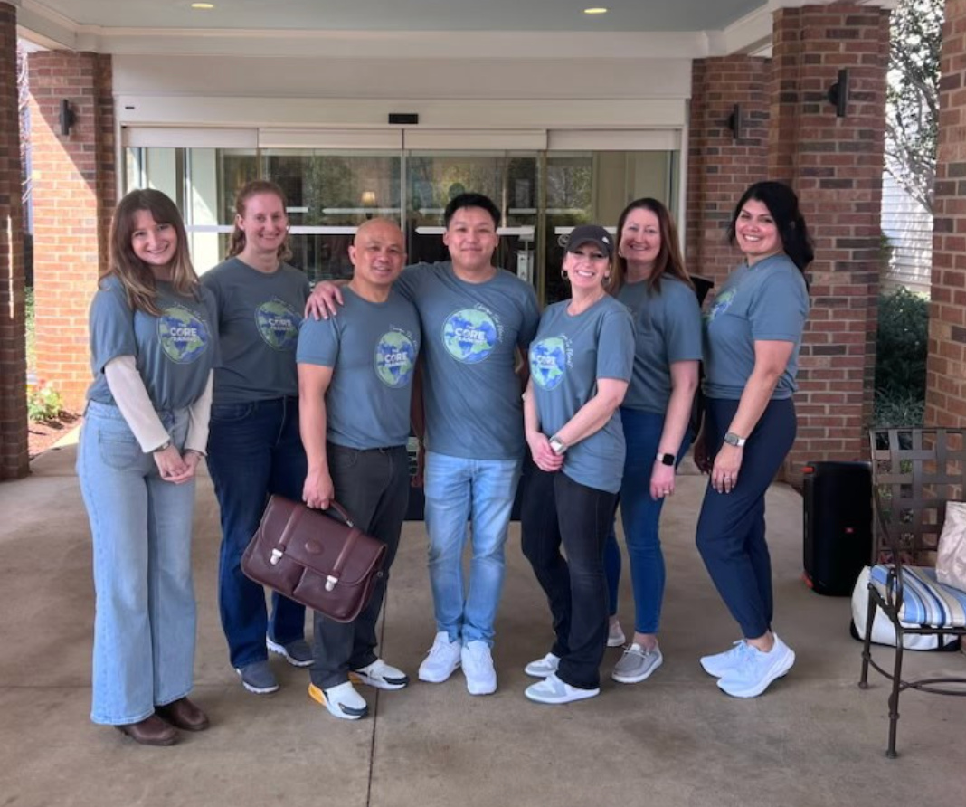 Group of seven people in matching gray shirts posing outside a building entrance