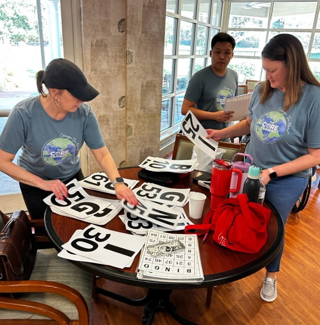 People sorting large black-and-white number signs on a table in a bright indoor room
