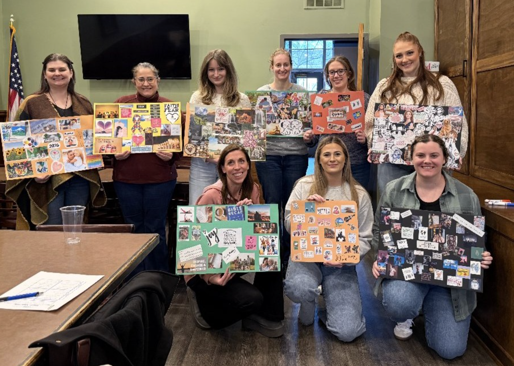 Group of people in a meeting room holding colorful collage boards and smiling at the camera.
