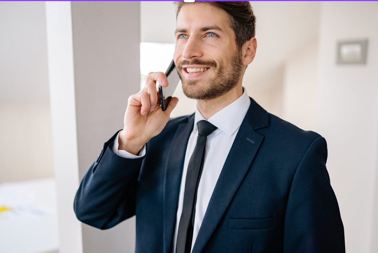 Smiling businessman in a dark suit talking on a phone indoors