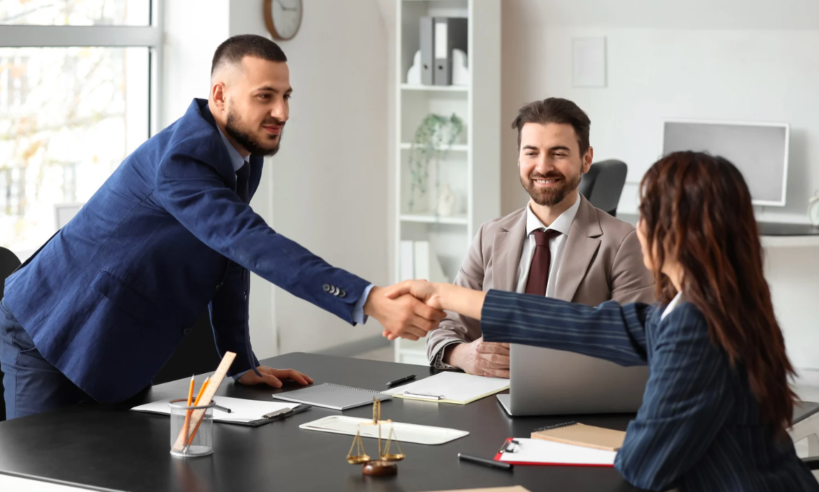 Business meeting with three colleagues shaking hands across a desk in a bright office