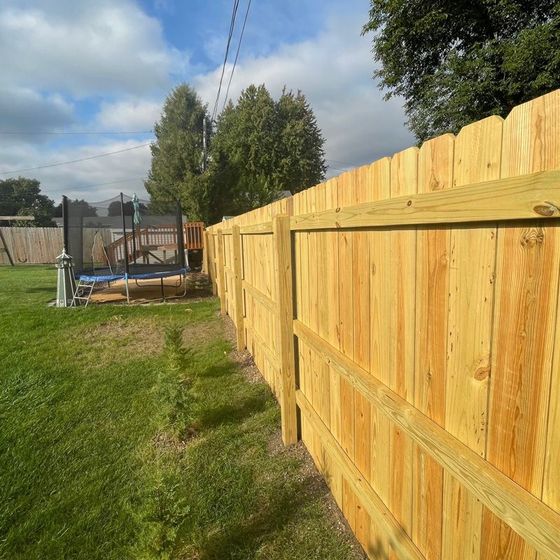 Wooden fence along a grassy yard beside a swimming pool under a partly cloudy sky