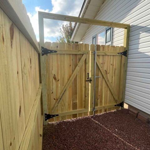 Wooden double gate with arched frame in a narrow side yard beside a white house and fence