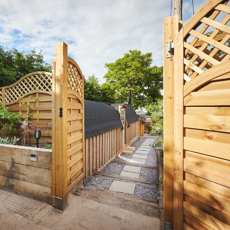 Wooden garden gate and fence opening to a gravel path with stepping stones and greenery.