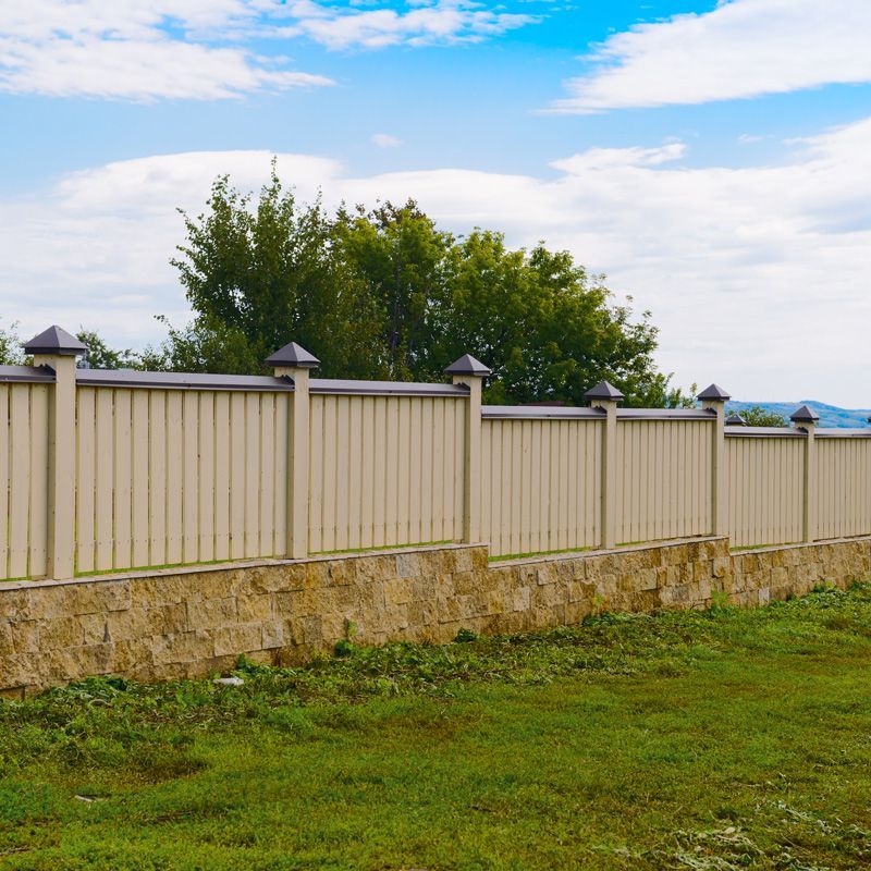 White fence with stone base along grassy yard under a partly cloudy sky